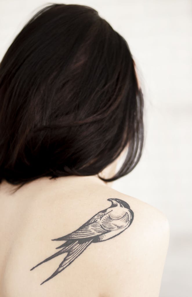 View of Woman's Back With Bird Tattoo on Right Shoulder