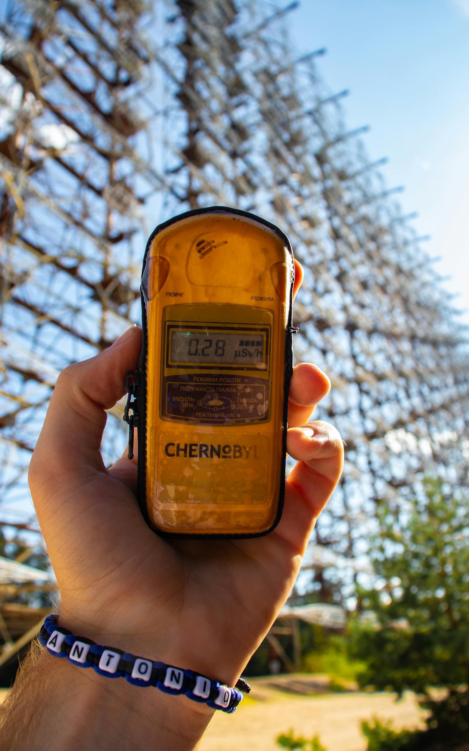Hand holding a dosimeter measuring radiation level at Chernobyl with Duga radar in background.