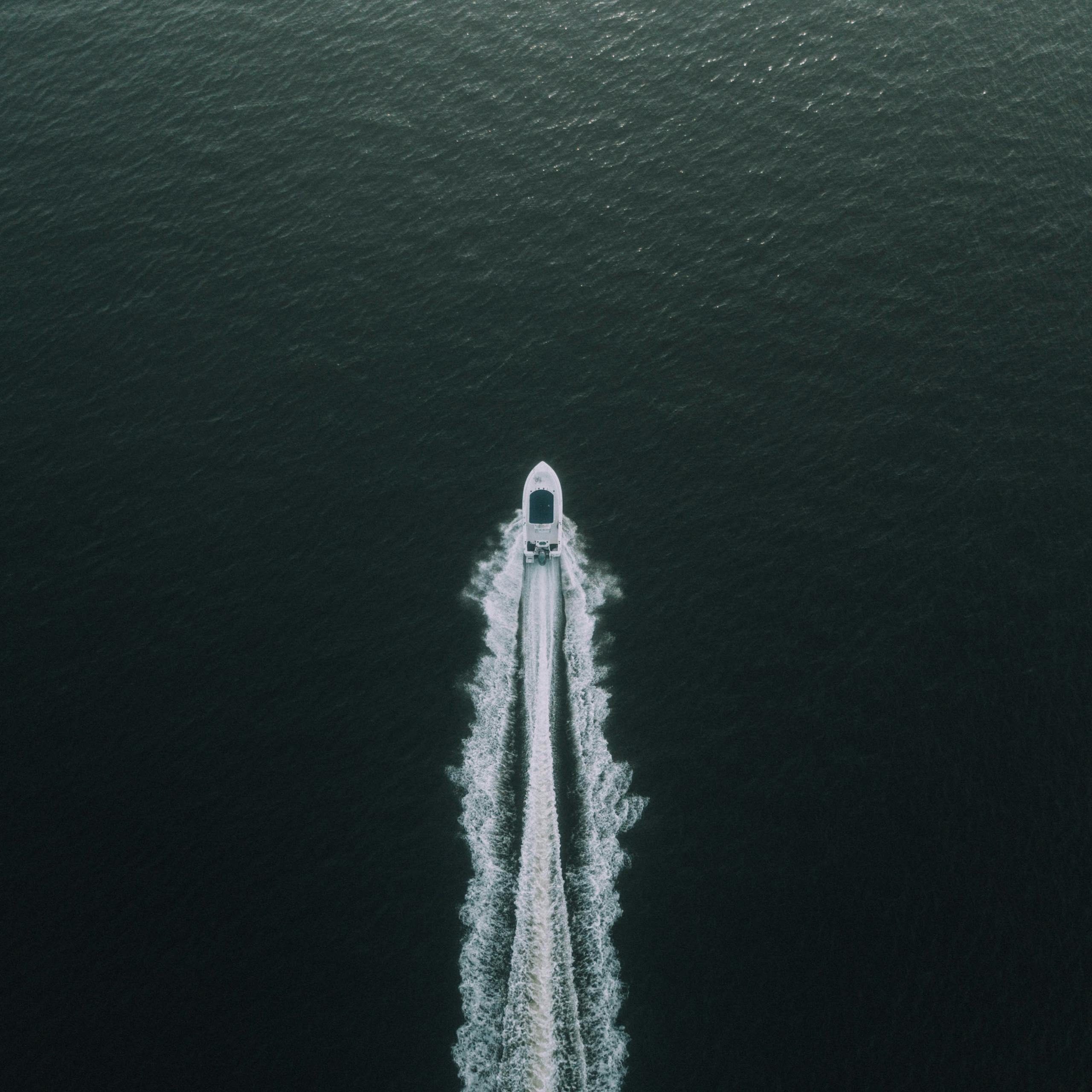 A high-angle shot of a boat creating ripples as it speeds across the tranquil sea, highlighting a peaceful maritime adventure.