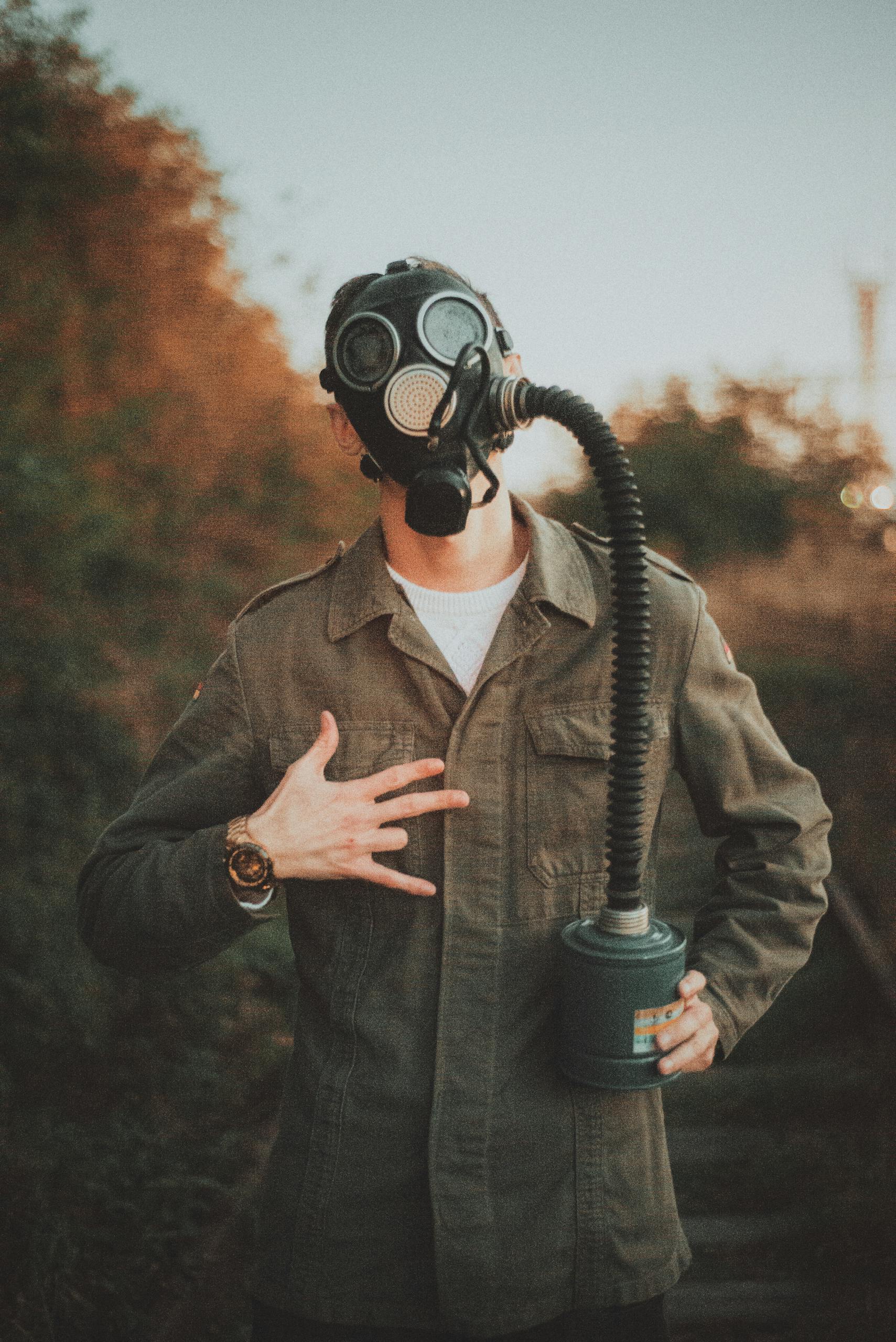 Individual wearing a gas mask standing outdoors depicting a post-apocalyptic scene.