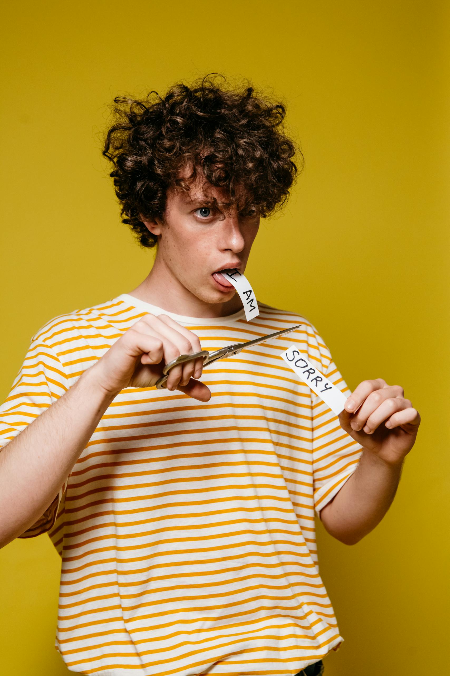 A young man using scissors to cut a paper note with 'I am sorry' against a yellow background.