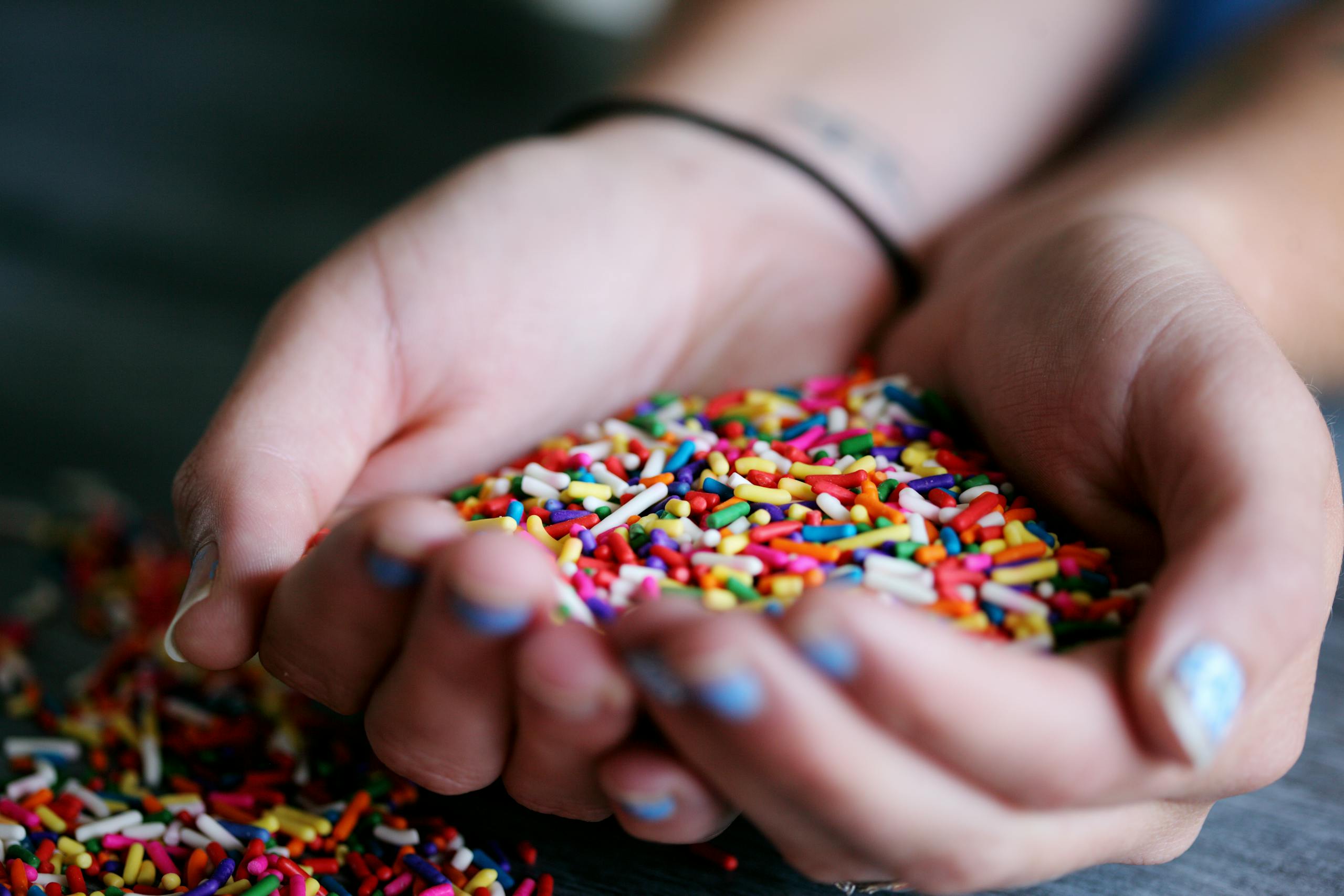 A close-up of hands holding a handful of colorful sprinkles over a dark surface.