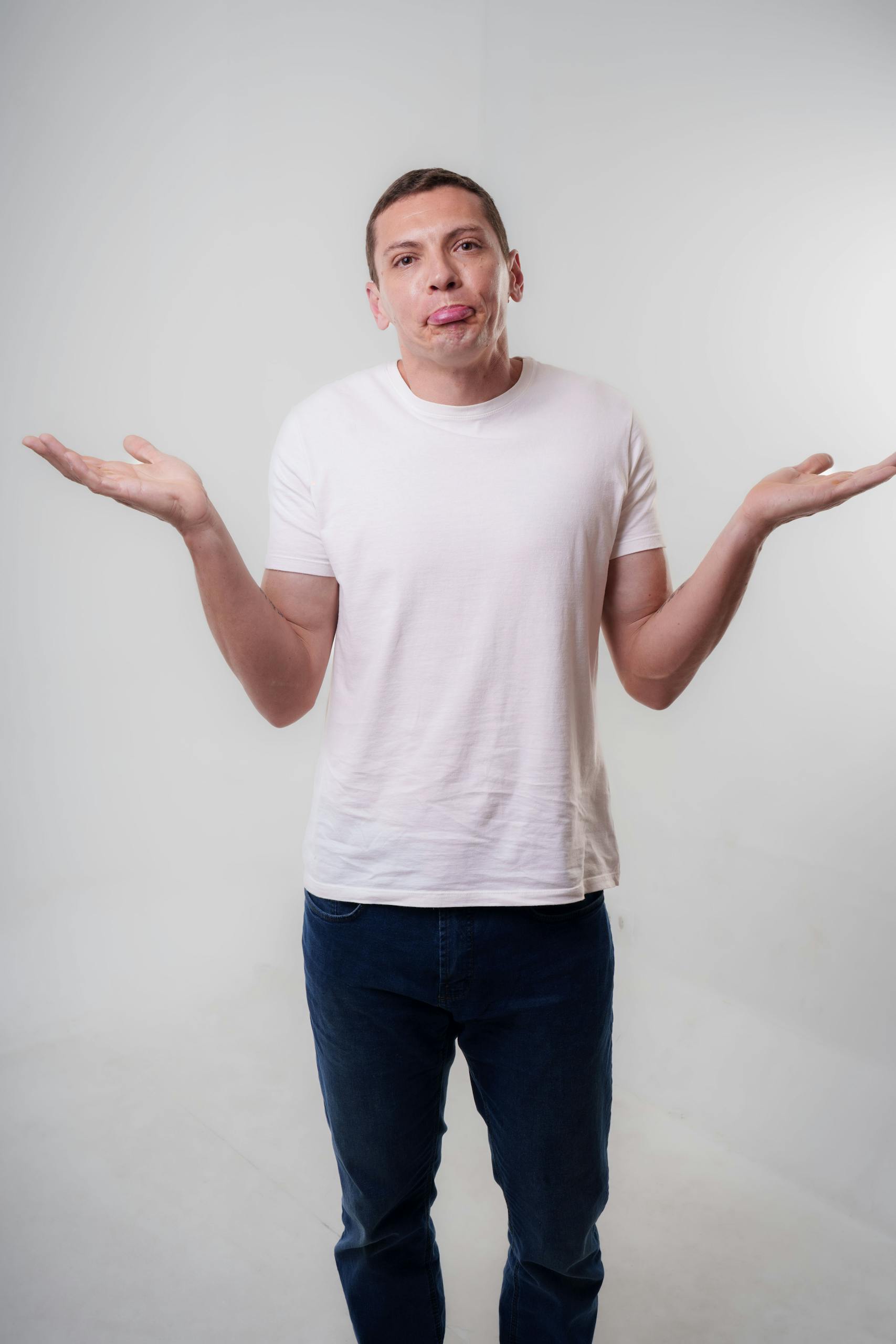 A young adult man in casual clothing shrugs with a neutral expression in a studio setting.