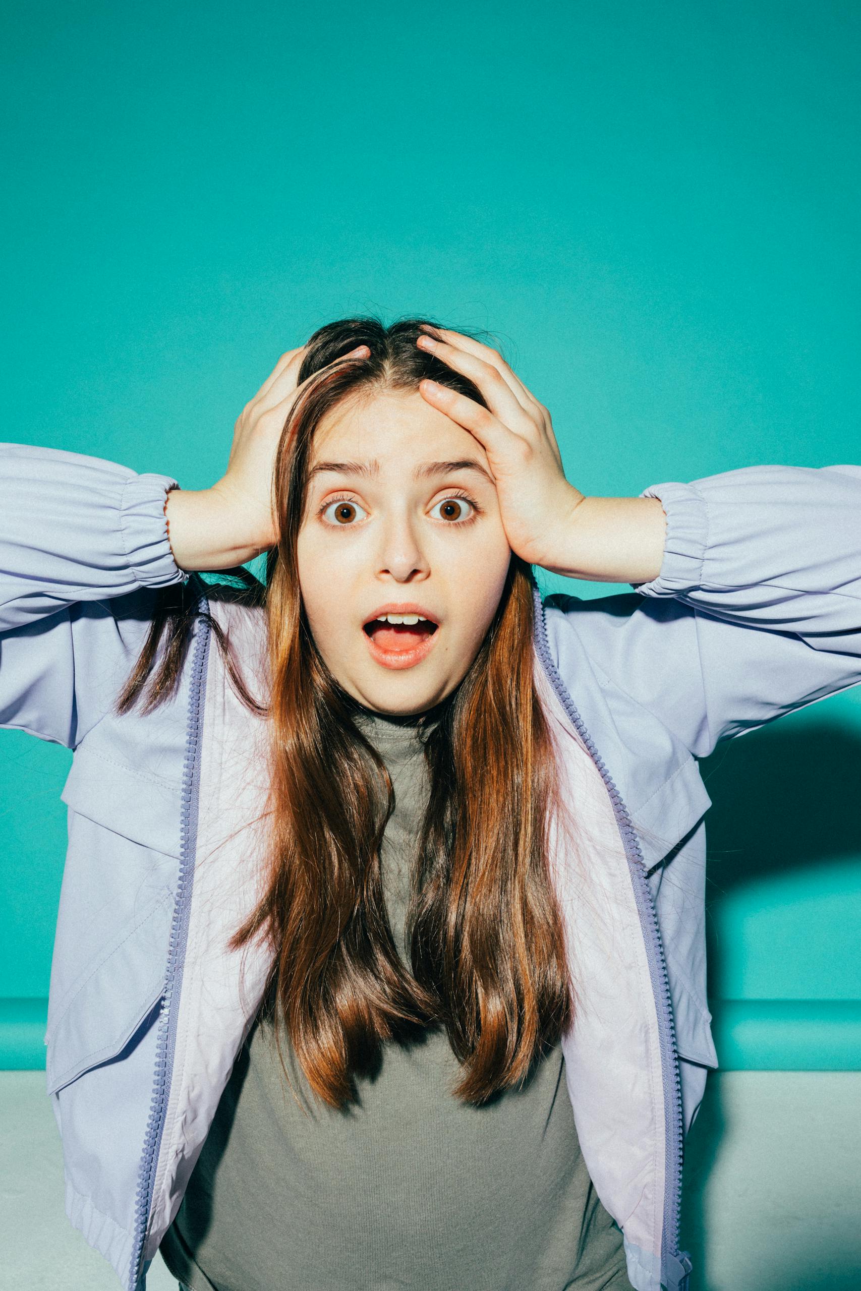 A young girl with a shocked expression holds her head against a vibrant background.