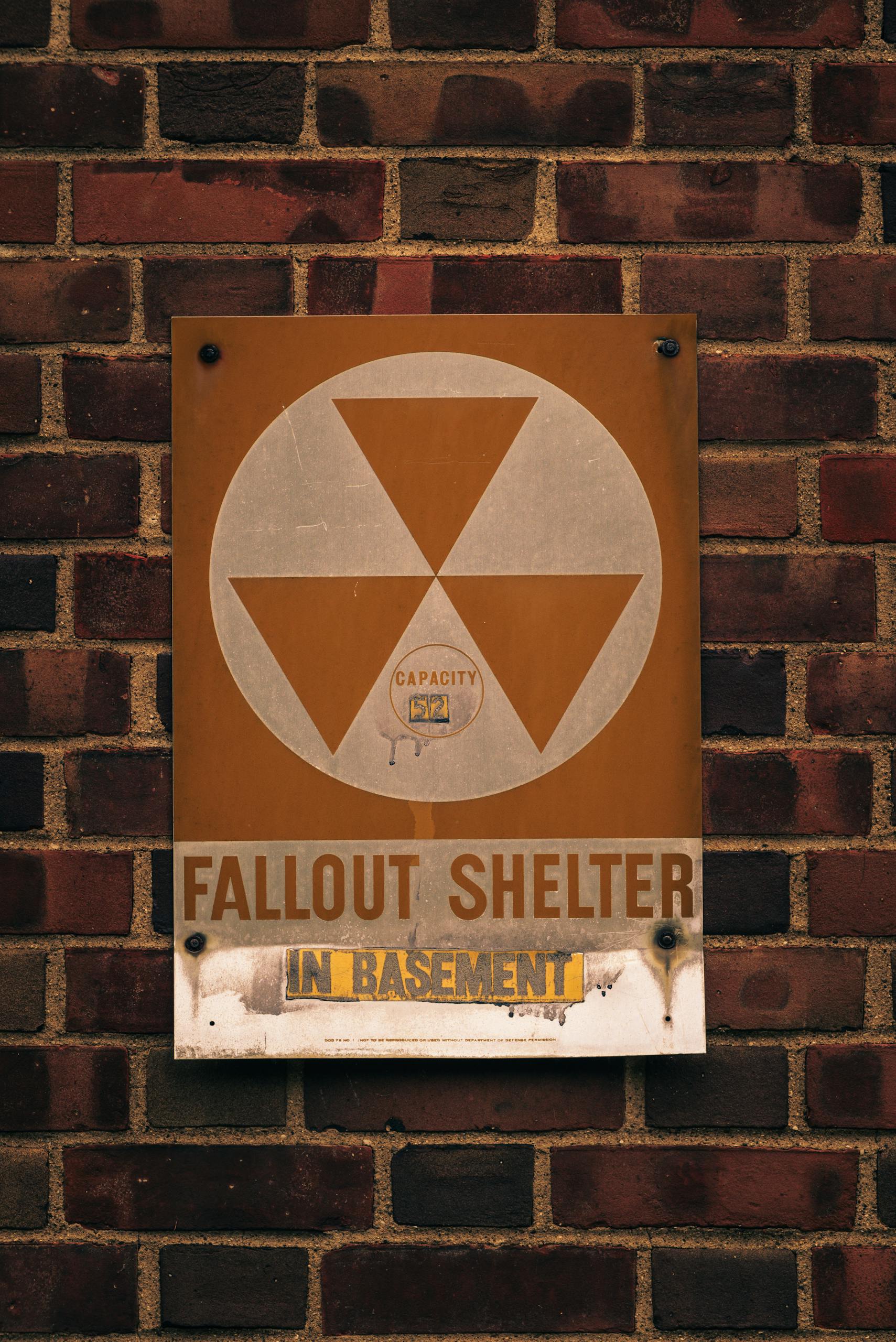 Rustic fallout shelter sign mounted on an aged brick wall.