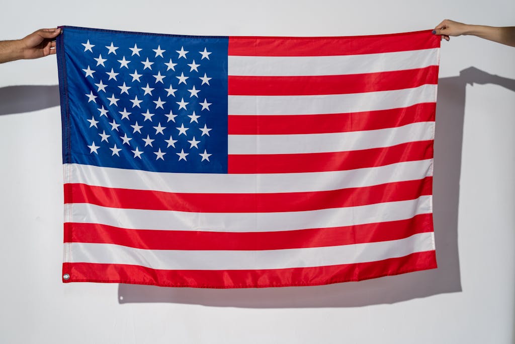 Two hands hold a vibrant American flag against a plain white wall.